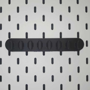 May include: Black plastic pegboard organiser with eight slots for holding tools or other items.