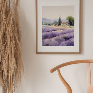 May include: A framed watercolor painting of a lavender field with a small house in the distance. The painting is in a light wood frame and is hanging on a white wall.