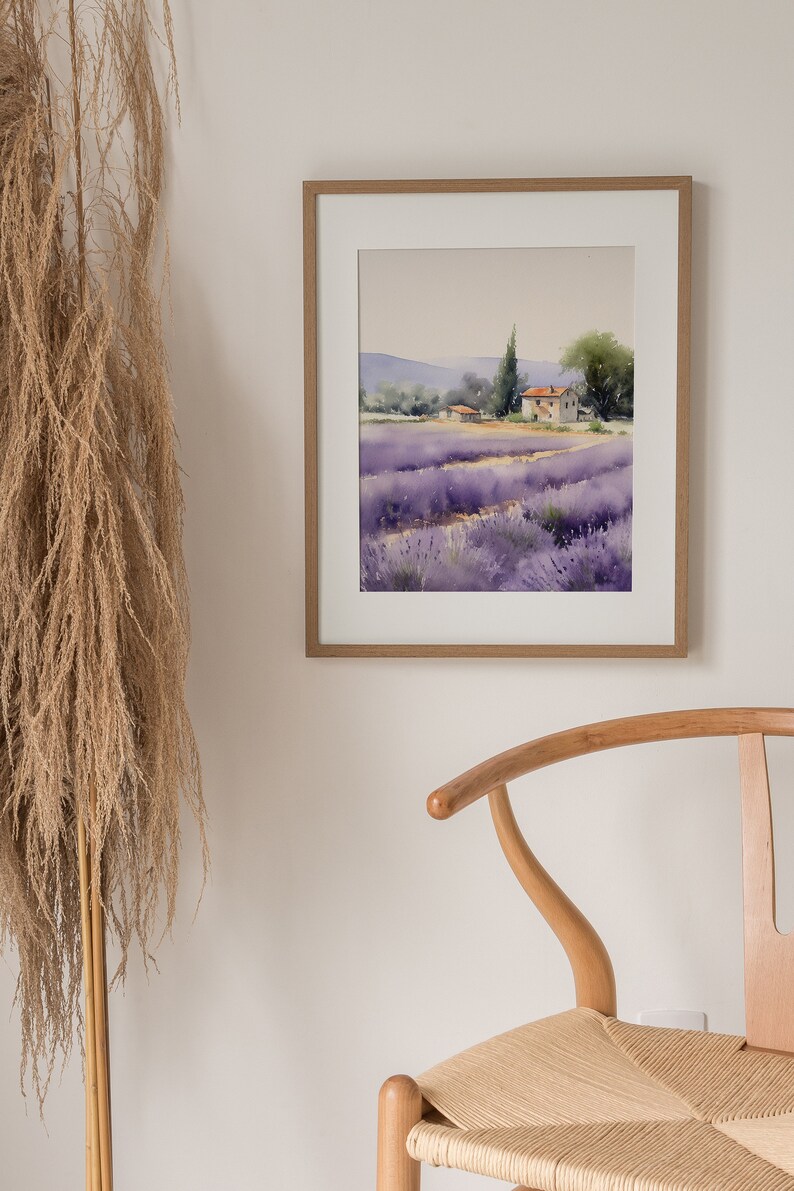 May include: A framed watercolor painting of a lavender field with a small house in the distance. The painting is in a light wood frame and is hanging on a white wall.