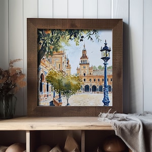 May include: A watercolour painting of a Spanish plaza with a clock tower and a street lamp. The painting is framed in a brown wooden frame and is hanging on a white wall.