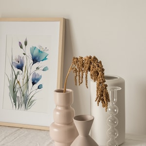 May include: A framed watercolor painting of blue flowers in a vase with dried flowers in a white vase and a pink vase on a white linen tablecloth.
