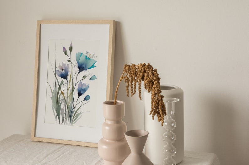May include: A framed watercolor painting of blue flowers in a vase with dried flowers in a white vase and a pink vase on a white linen tablecloth.