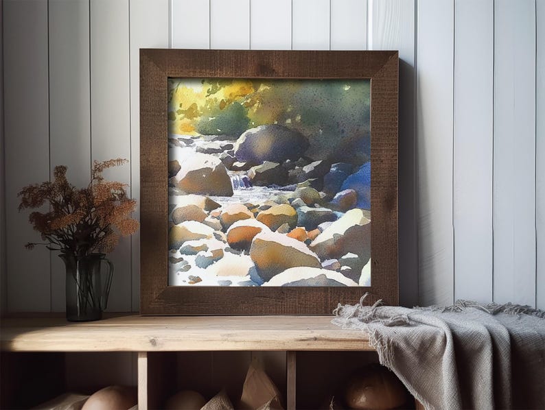 May include: A framed watercolor painting of a stream flowing over rocks in a forest. The painting is in a brown wooden frame and is hanging on a white wall.