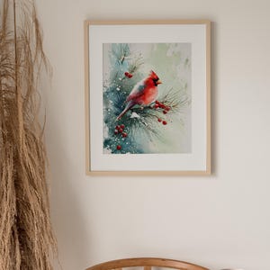 Op de afbeelding: Waterverfschilderij van een rode kardinaal die op een met sneeuw bedekte dennentak met rode bessen zit. Het kunstwerk is ingelijst in een licht houten frame, waardoor een serene winterse sc&egrave;ne ontstaat. Het schilderij wordt in een goed verlichte ruimte tentoongesteld.
