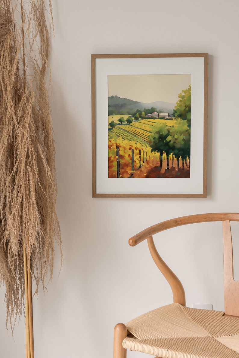 Puede incluir: Una pintura de acuarela enmarcada de un paisaje de vi&ntilde;edo con hileras de vides, una granja en la distancia y un cielo azul con nubes. La pintura est&aacute; en un marco de madera claro.