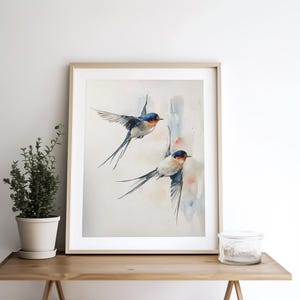 May include: Watercolor painting of two blue and white swallows in flight against a light blue and pink background.