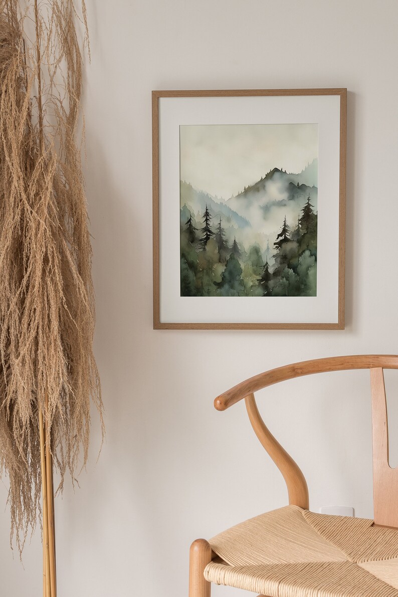 Pu&ograve; includere: Un dipinto ad acquerello incorniciato che rappresenta una scena di foresta nebbiosa con alberi verdi e montagne. Il dipinto &egrave; in una cornice di legno chiaro ed &egrave; appeso a una parete bianca.