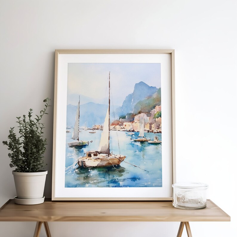 May include: A watercolour painting of a sailboat on a calm blue sea with a cityscape in the background. The sailboat has a white sail and a brown hull. The cityscape is made up of buildings with red roofs and green trees. The painting is framed in a light wood frame.
