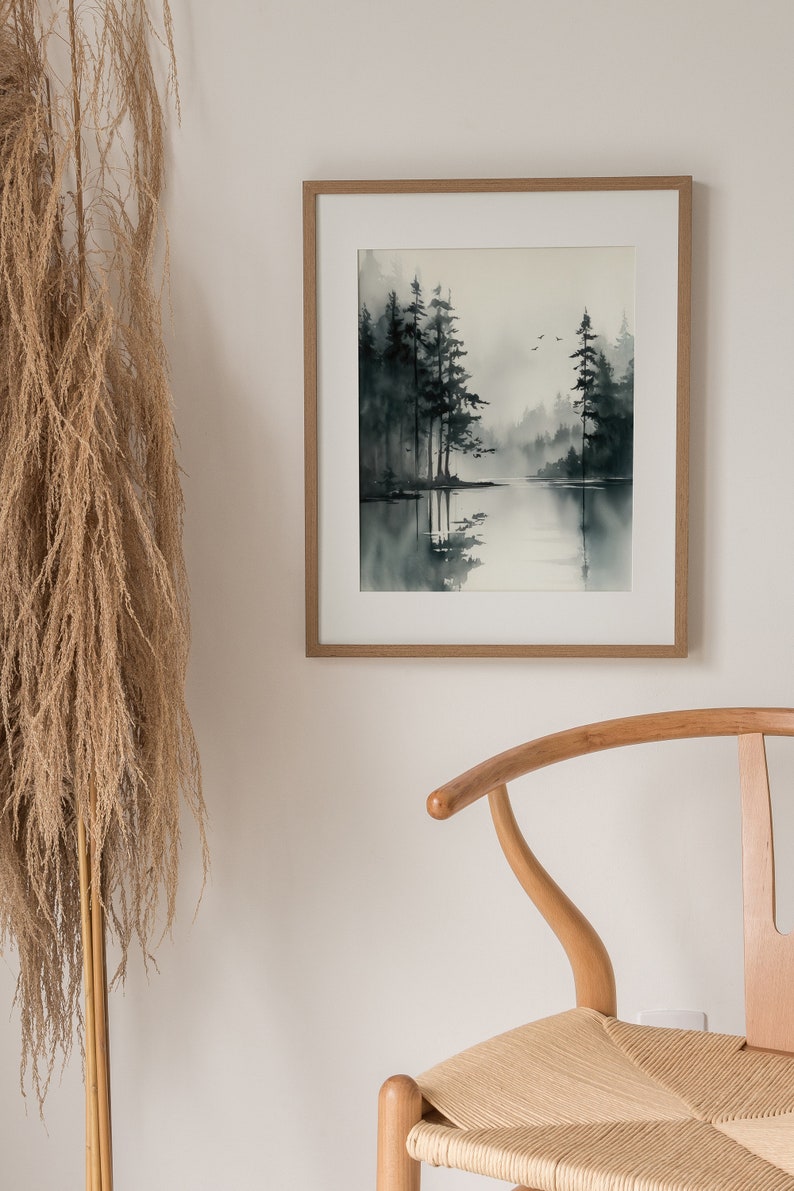 May include: A framed watercolor painting of a misty forest scene with a lake in the foreground. The trees are dark green and the water is a light blue. The painting is in a light wood frame.