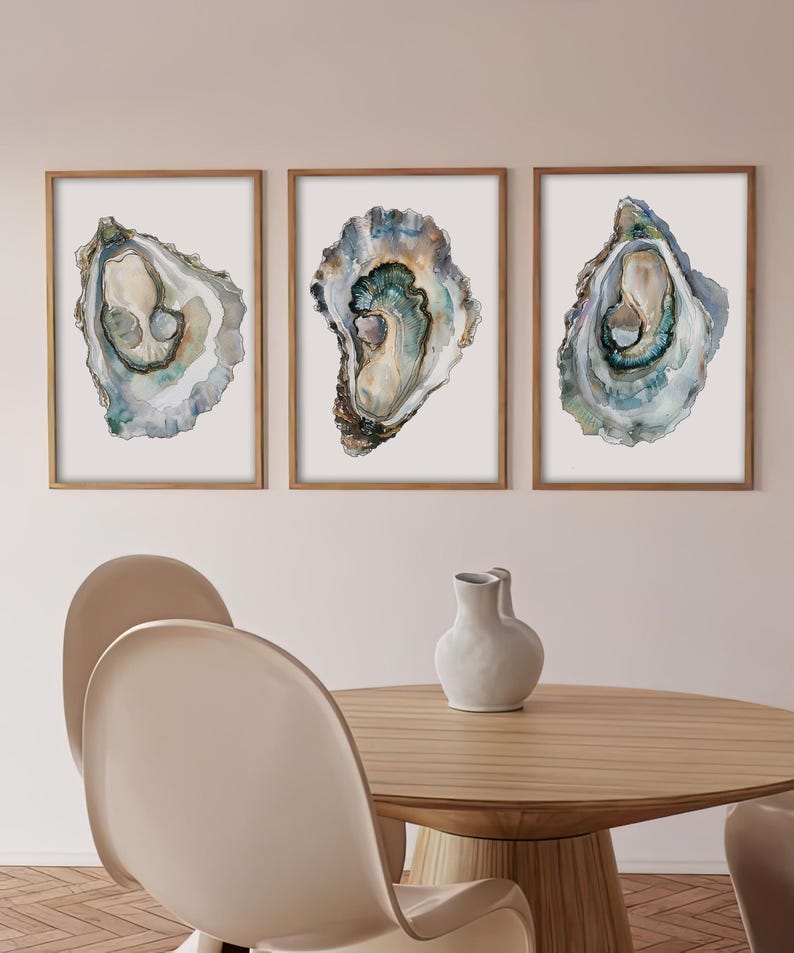 May include: Three watercolor paintings of oyster shells in shades of blue, green, and brown. The paintings are framed in natural wood frames and are displayed on a white wall.