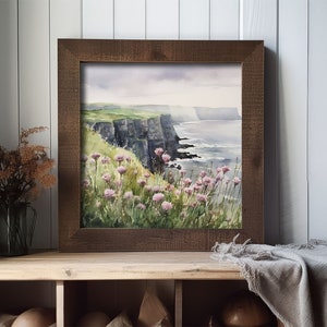 K&ouml;nnte beinhalten: Ein gerahmtes Aquarellbild einer K&uuml;stenlandschaft mit gr&uuml;nen Klippen, einem blauen Meer und rosa Wildblumen im Vordergrund.