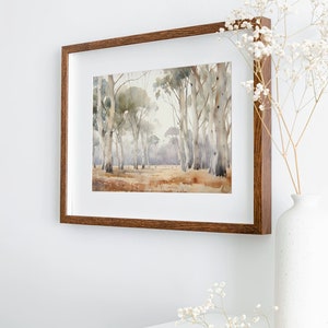 May include: A framed watercolour painting of a woodland scene with tall, slender trees in shades of brown and grey. The painting is in a brown wooden frame and is hanging on a white wall.