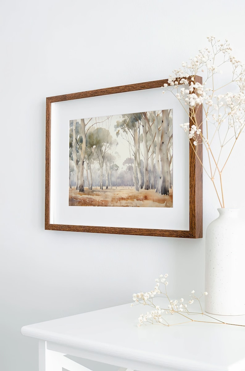 May include: A framed watercolour painting of a woodland scene with tall, slender trees in shades of brown and grey. The painting is in a brown wooden frame and is hanging on a white wall.