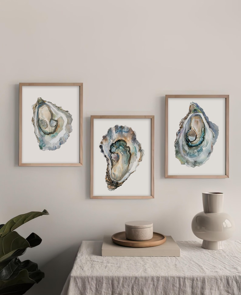 May include: Three framed watercolor paintings of oyster shells. The oyster shells are painted in shades of blue, green, and brown. The frames are a light wood color.