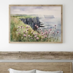 K&ouml;nnte beinhalten: Aquarellgem&auml;lde einer Klippe, die &uuml;ber einem Gew&auml;sser thront. Die Klippe ist gr&uuml;n und braun mit einer felsigen Textur. Das Wasser ist blau und hat wei&szlig;e Wellen. Im Vordergrund befinden sich rosa Blumen.