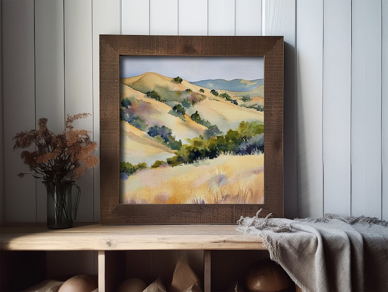 May include: Watercolor painting of rolling hills with green trees and yellow grass. The painting is framed in a dark brown wood frame.