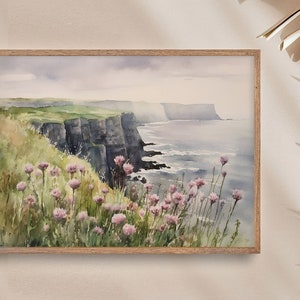 K&ouml;nnte beinhalten: Aquarellmalerei einer K&uuml;stenlandschaft mit dramatischen Klippen und einem Meer im Hintergrund. Im Vordergrund befindet sich ein Feld mit rosa Wildblumen.