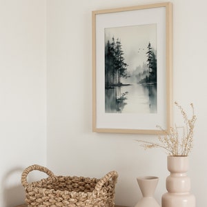 May include: A framed watercolor painting of a lake scene with trees and a misty background. The painting is hanging on a white wall above a wooden dresser with a woven basket and two ceramic vases.