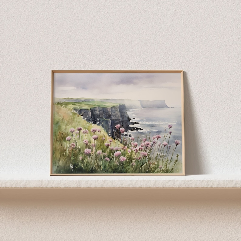 K&ouml;nnte beinhalten: Aquarellgem&auml;lde einer Klippenlandschaft mit Blick auf das Meer. Das Gem&auml;lde zeigt eine felsige Klippe mit gr&uuml;nem Gras und rosa Wildblumen im Vordergrund. Das Meer ist hellblau mit wei&szlig;en Wellen.