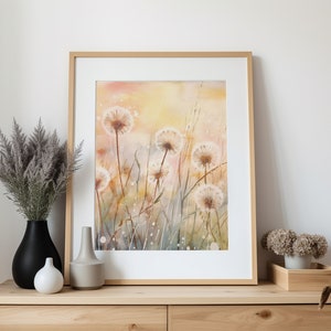 May include: A framed watercolor painting of a field of white dandelions with a soft yellow and orange background. The painting is in a light wood frame and is hanging on a white wall.