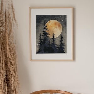 May include: Watercolor painting of a night scene with a large, golden moon and silhouetted pine trees. The artwork is framed in a light wood frame and hangs on a neutral-colored wall. The overall theme is nature and landscape.