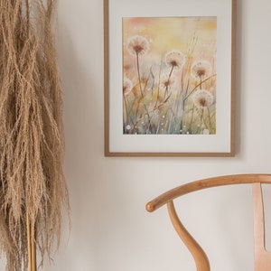 May include: A framed watercolor painting of a field of white dandelions with a soft, yellow background. The painting is in a light wood frame.