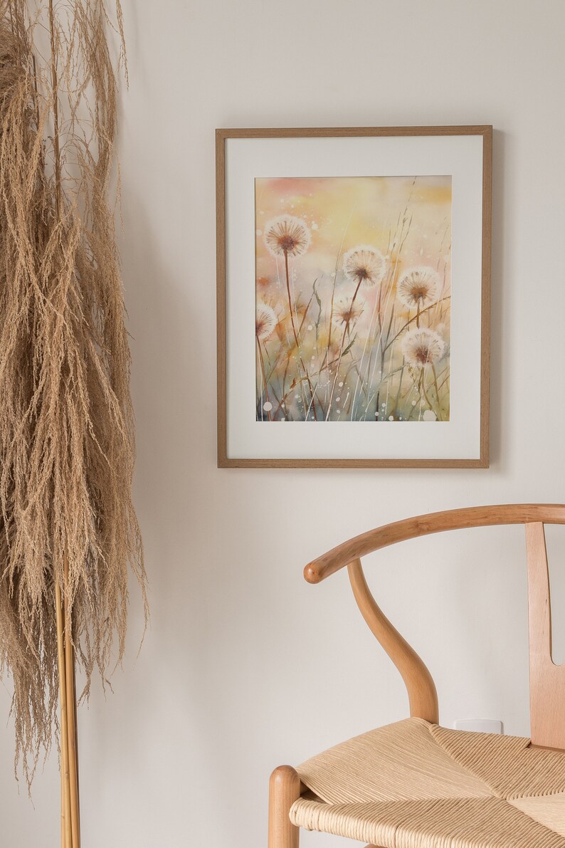 May include: A framed watercolor painting of a field of white dandelions with a soft, yellow background. The painting is in a light wood frame.