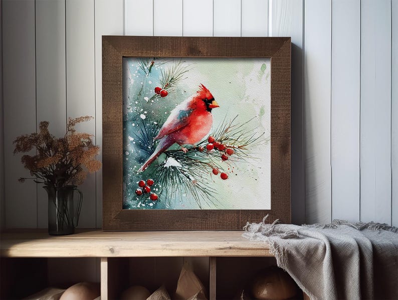 Op de afbeelding: Waterverfschilderij van een rode kardinaal op een dennentak met rode bessen, tegen een besneeuwde, lichtblauwe achtergrond. Het kunstwerk is ingelijst in een donkerbruine houten lijst. De schildering wordt tentoongesteld op een houten plank.