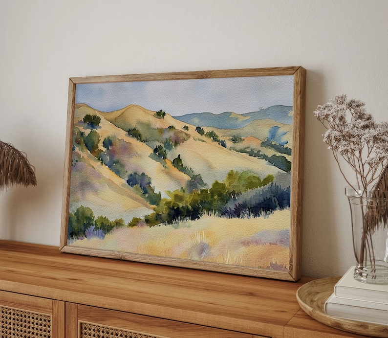 May include: Watercolor painting of a landscape with rolling hills, green trees, and a blue sky. The hills are painted in shades of yellow, brown, and green. The trees are painted in shades of green and blue. The sky is painted in shades of blue and white.