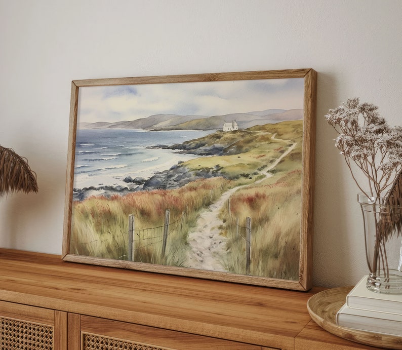 May include: A watercolour painting depicting a coastal scene with a white house on a cliff overlooking a rocky beach and a winding path leading to it.