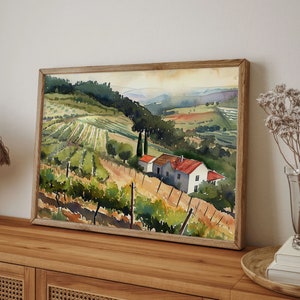 May include: Watercolor painting of a vineyard landscape with rolling hills, a farmhouse, and a wooden frame. The artwork features green and brown tones, with a focus on the rows of grapevines and the rural setting. The painting is displayed on a wooden surface.
