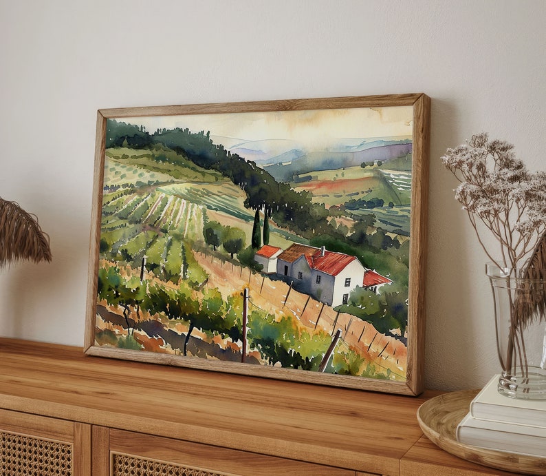 May include: Watercolor painting of a vineyard landscape with rolling hills, a farmhouse, and a wooden frame. The artwork features green and brown tones, with a focus on the rows of grapevines and the rural setting. The painting is displayed on a wooden surface.