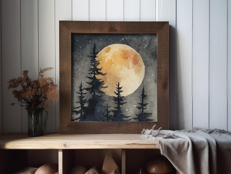 May include: Watercolor painting of a full moon over a forest of silhouetted pine trees. The artwork is framed in a dark brown wooden frame. The moon is a warm yellow color, and the sky is a dark gray with small white stars.