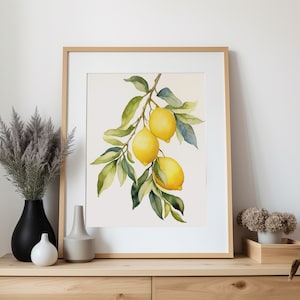 Op de afbeelding: Een aquarel van een citroen tak met drie citroenen. De citroenen zijn geel met groene bladeren. Het schilderij is ingelijst in een licht houten lijst.
