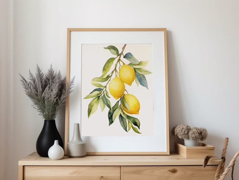 Op de afbeelding: Een aquarel van een citroen tak met drie citroenen. De citroenen zijn geel met groene bladeren. Het schilderij is ingelijst in een licht houten lijst.