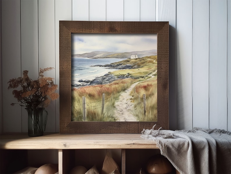 May include: A framed watercolour painting of a coastal scene with a white house on a hill overlooking a rocky beach and a path leading to it.