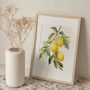 Op de afbeelding: Een ingelijst aquarel schilderij van een citroen tak met drie citroenen. De citroenen zijn geel en de bladeren zijn groen. De lijst is van licht hout en het schilderij heeft een witte achtergrond.