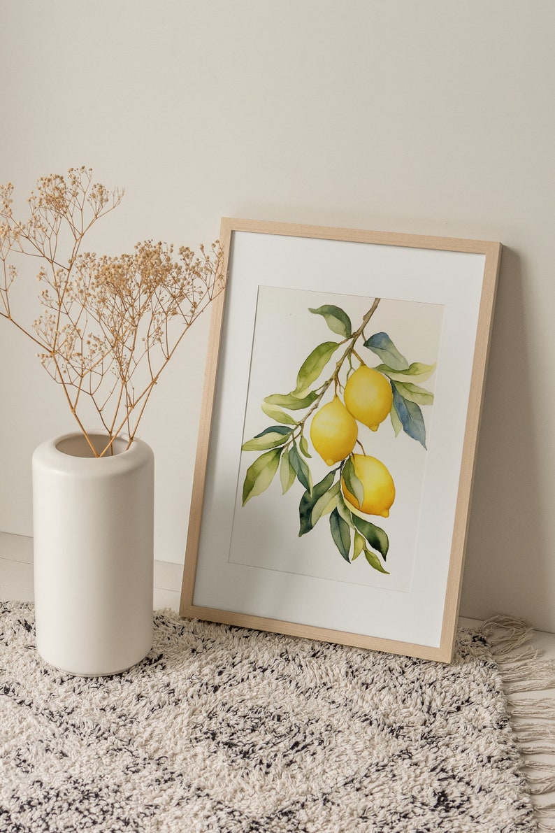 Op de afbeelding: Een ingelijst aquarel schilderij van een citroen tak met drie citroenen. De citroenen zijn geel en de bladeren zijn groen. De lijst is van licht hout en het schilderij heeft een witte achtergrond.