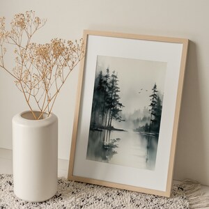 May include: A framed watercolor painting of a misty forest scene with a lake in the foreground. The trees are dark green and the water is a light blue. The painting is in a light wood frame.