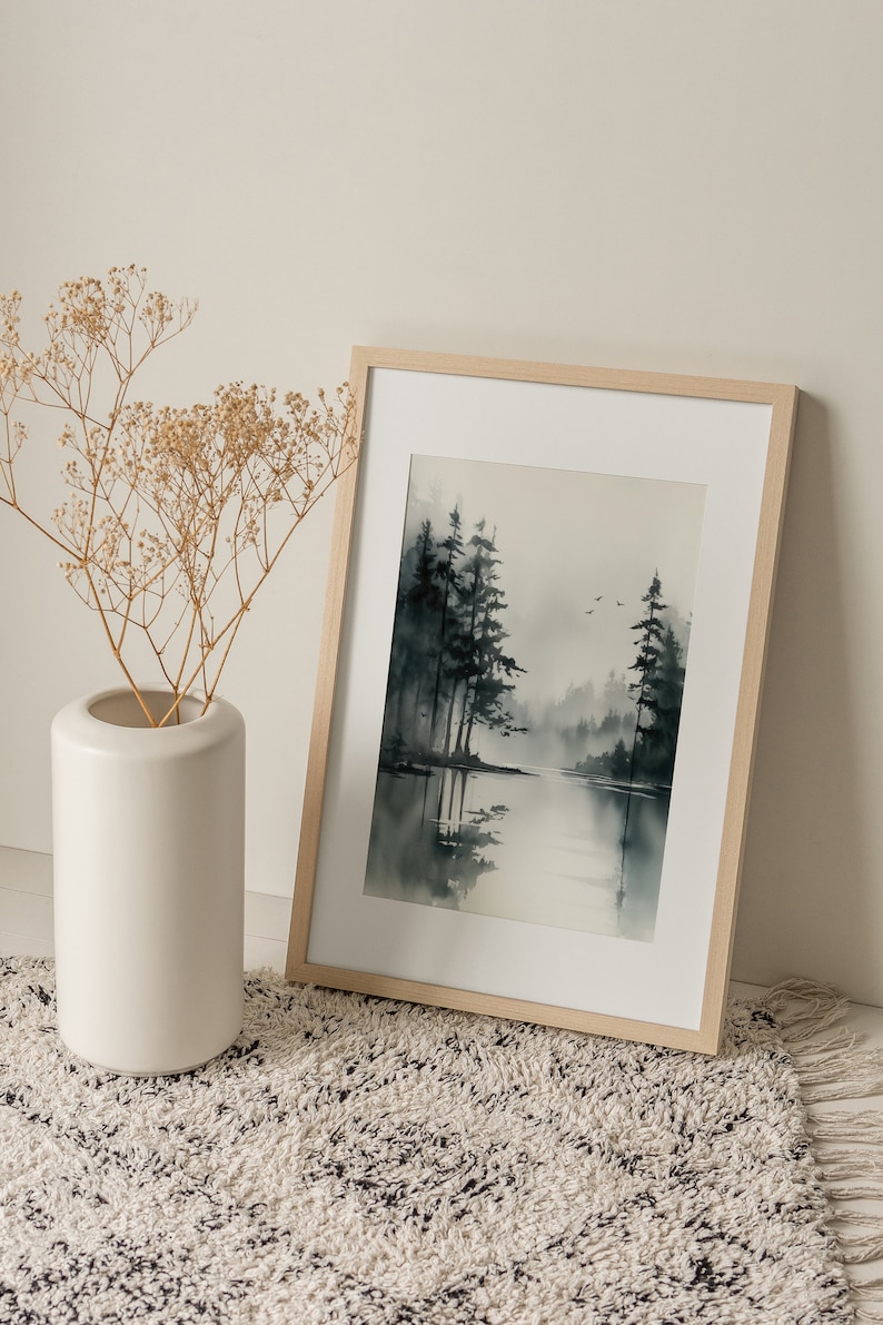 May include: A framed watercolor painting of a misty forest scene with a lake in the foreground. The trees are dark green and the water is a light blue. The painting is in a light wood frame.