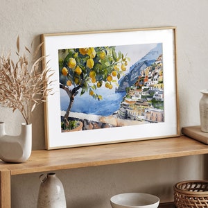 May include: A framed watercolor painting of a lemon tree with yellow lemons and green leaves in front of a colorful cityscape on a cliff overlooking a blue body of water.