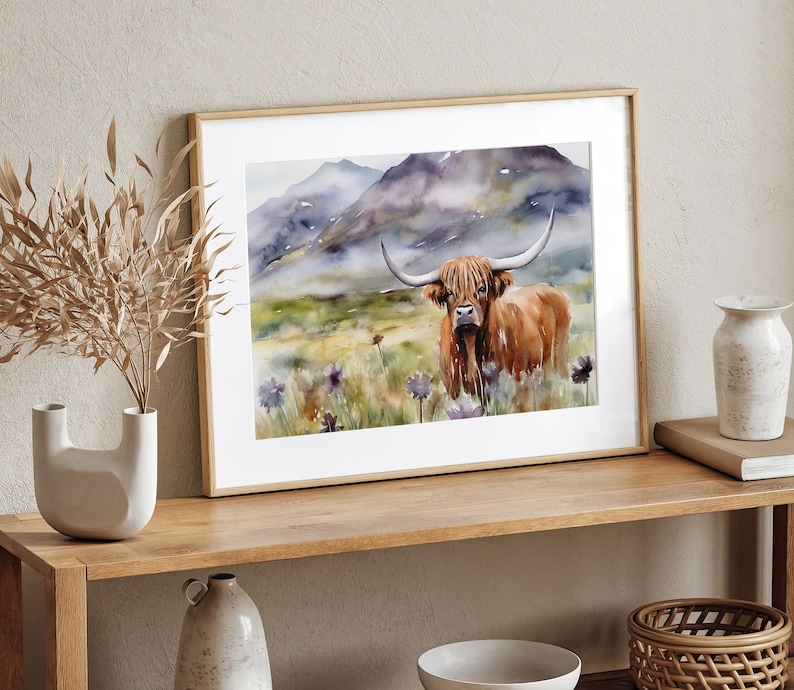 May include: A watercolor painting of a Highland cow standing in a field of wildflowers. The cow is brown and white with long horns. The background is a misty mountain landscape.