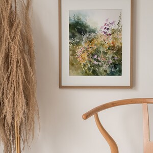 May include: A framed watercolor painting of a field of wildflowers in shades of purple, yellow, and green. The painting is set against a white wall with a wooden chair in the foreground.