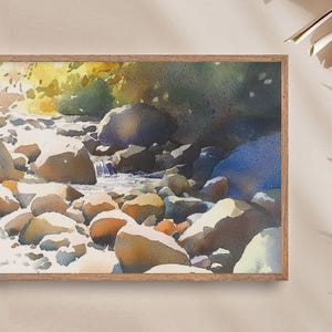 May include: Watercolor painting of a stream flowing through a rocky landscape. The water is a light blue, and the rocks are a variety of browns and grays. The painting is framed in a light wood frame.
