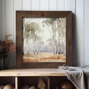 May include: A framed watercolour painting of a woodland scene with tall trees and a light brown background. The frame is a dark brown wood.