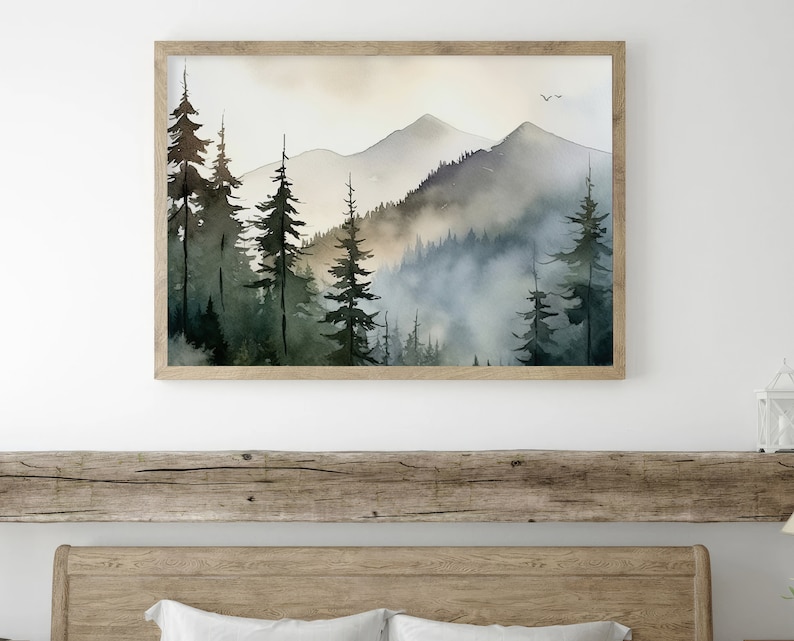 May include: A watercolor painting of a misty mountain landscape with a forest of pine trees in the foreground. The painting is framed in a light wood frame.