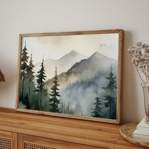 May include: A framed watercolor painting of a misty mountain landscape with a forest of evergreen trees in the foreground. The painting is in shades of blue, green, and brown.