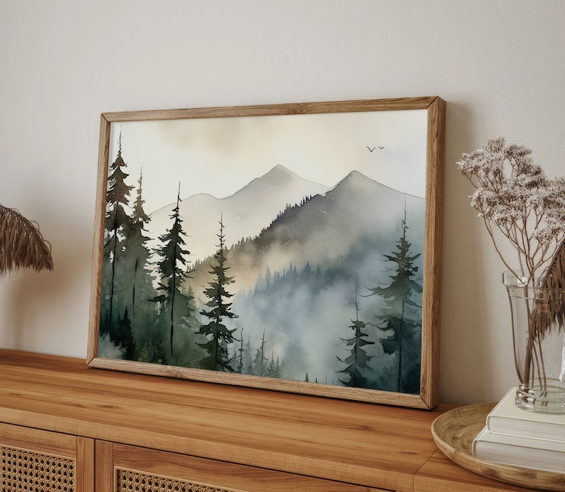 May include: A framed watercolor painting of a misty mountain landscape with a forest of evergreen trees in the foreground. The painting is in shades of blue, green, and brown.