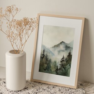 Pu&ograve; includere: Un dipinto ad acquerello incorniciato che rappresenta una scena di foresta nebbiosa con una montagna sullo sfondo. Il dipinto &egrave; in una cornice di legno chiaro e si trova su un tappeto bianco e nero.