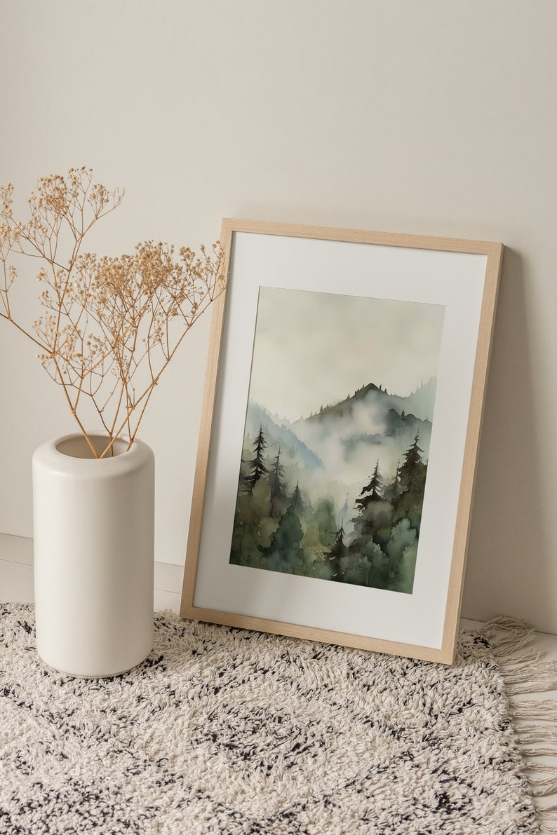 Pu&ograve; includere: Un dipinto ad acquerello incorniciato che rappresenta una scena di foresta nebbiosa con una montagna sullo sfondo. Il dipinto &egrave; in una cornice di legno chiaro e si trova su un tappeto bianco e nero.